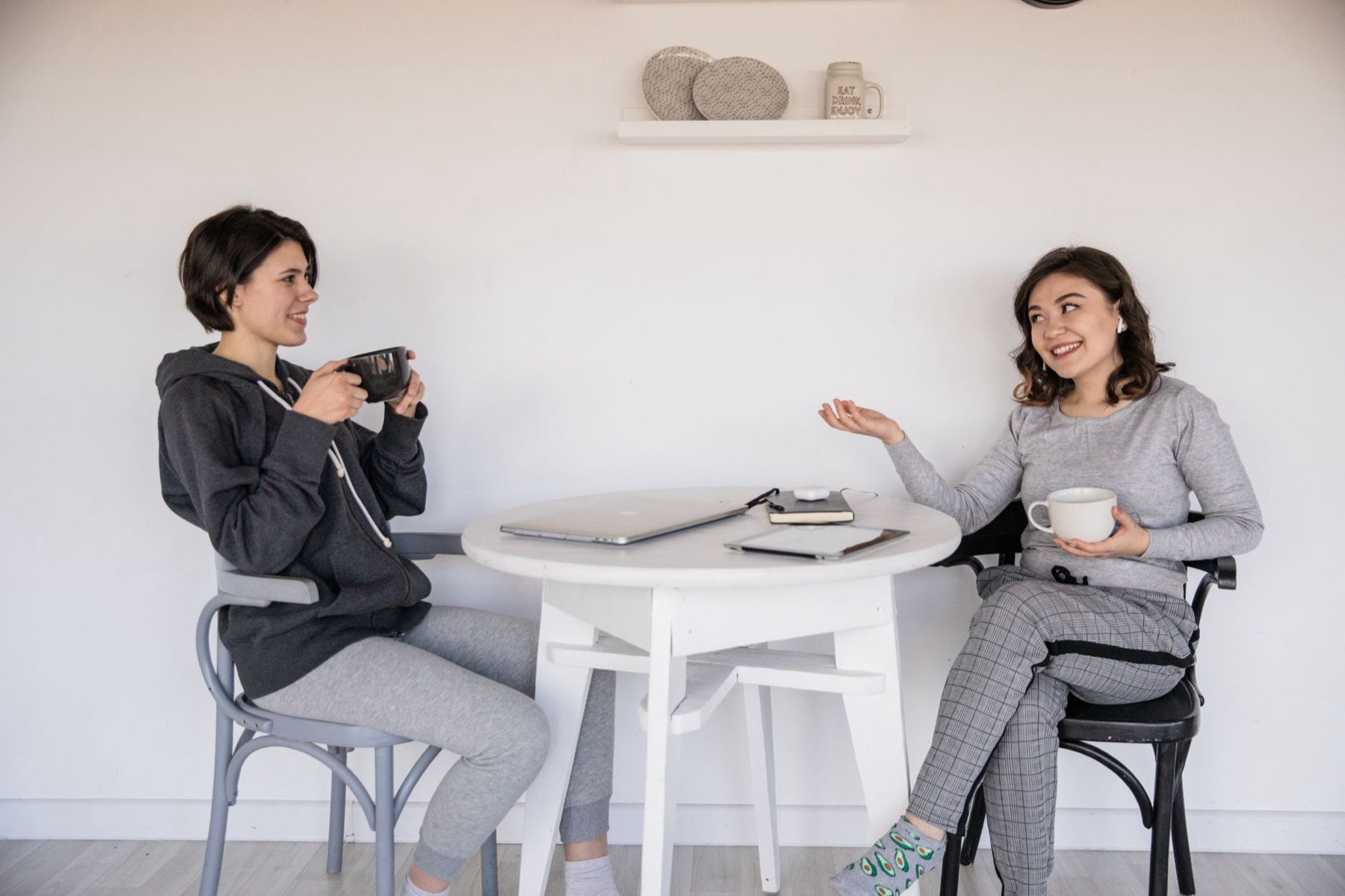 To kvinder griner over en kop kaffe ved et bord med en laptop