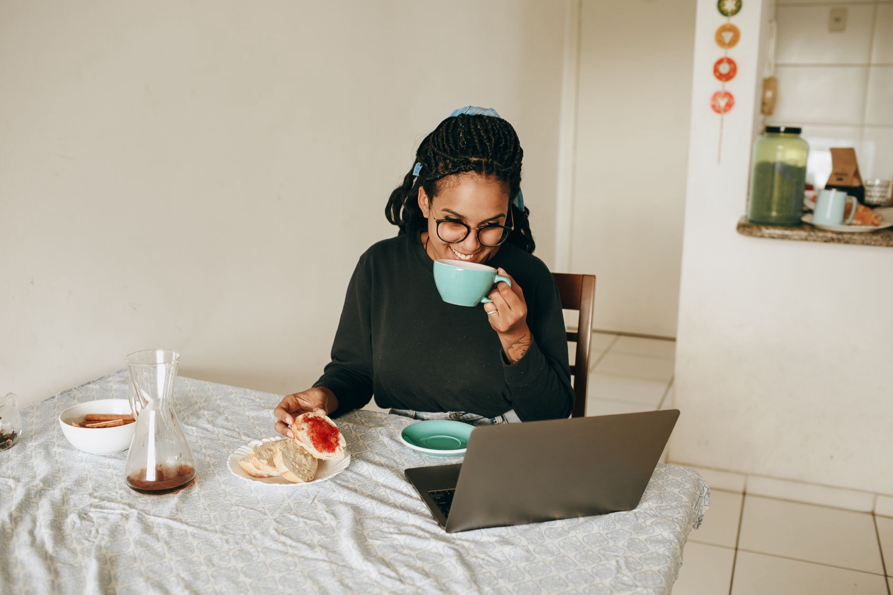 Kvinde med kaffe og laptop ved et køkkenbord